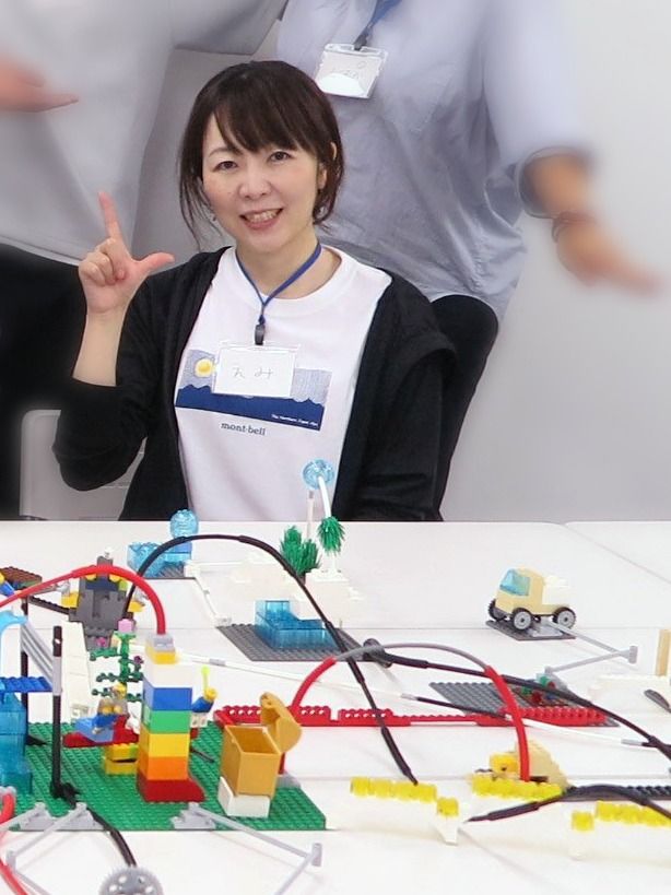 ワークショップの机に並んだレゴ作品の前に立つ谷口絵美